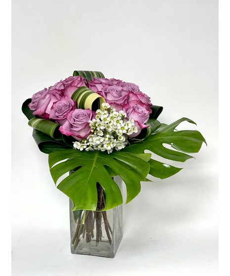 One dozen purple roses in a clear glass vase.